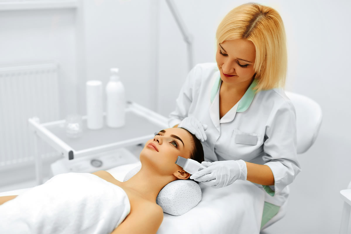 kosmetolog przeprowadza kobiecy peeling kawitacyjny w klinice urody